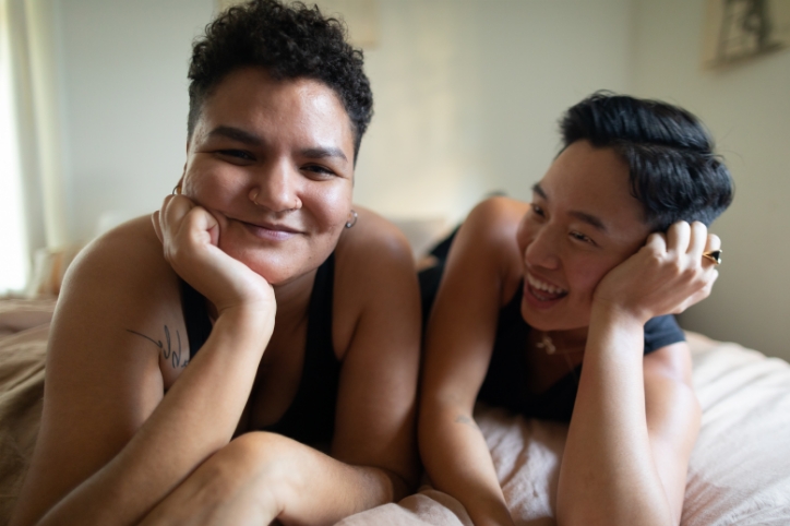 Two casual, happy women laying on top of a bed together