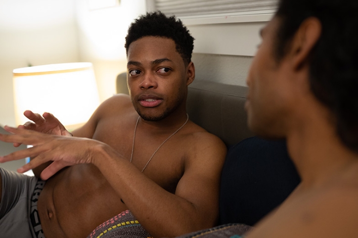 Two men sitting up in bed and having a serious conversation