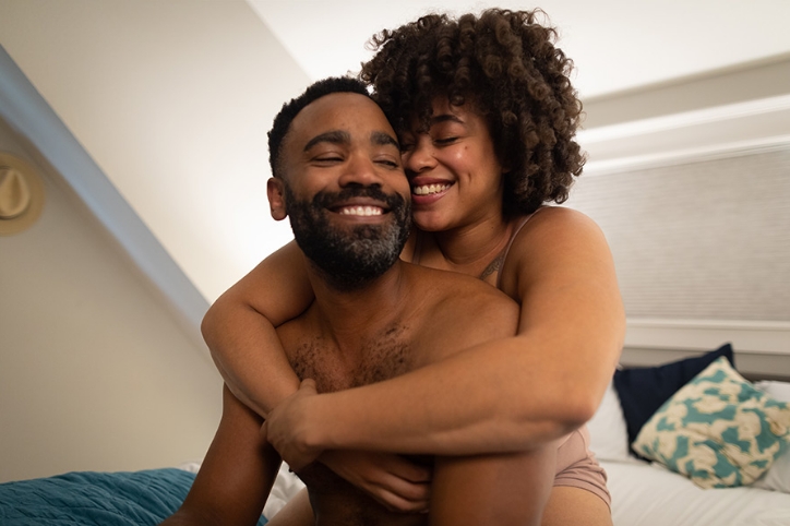 Straight black couple sitting on a bed and hugging