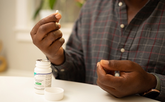 Hand holding a pill next to a medication bottle
