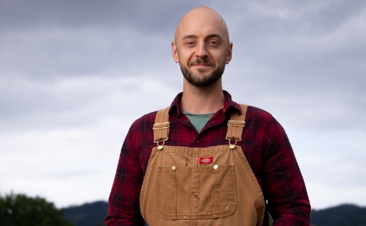 Portrait of a white man in his 30s with overalls and a flannel shirt