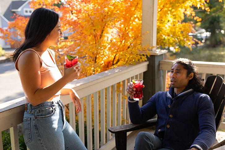 Two people talking together. They are drinking juice on a porch.